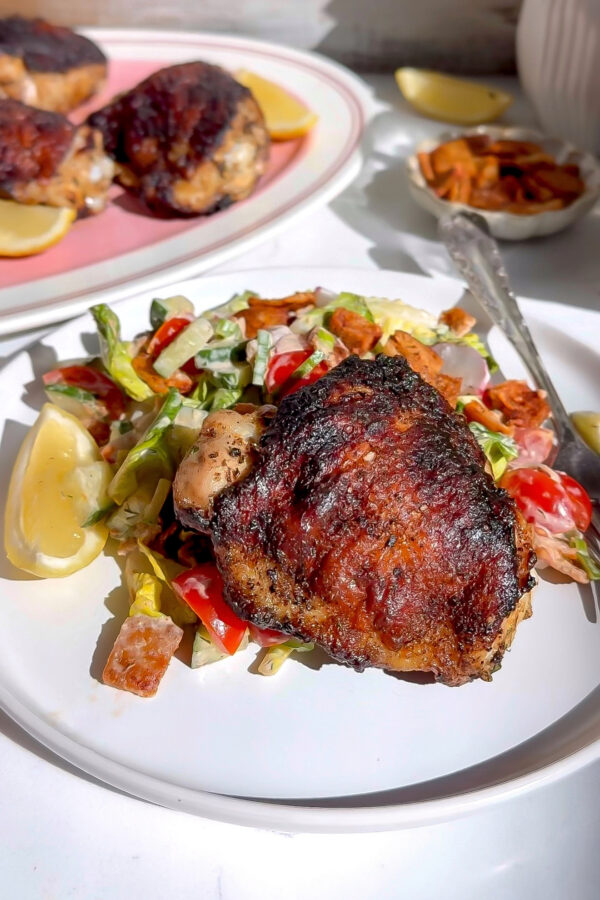 A recipe for Chipotle Ranch Marinated Chicken thighs nice and crispy off the grill sitting on a bed of salad with a lemon next to it.