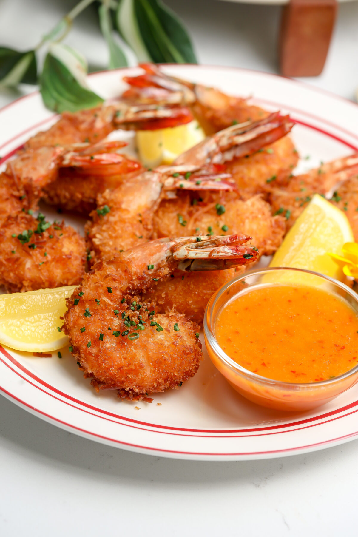 Crispy coconut shrimp with a sweet and spicy chili sauce sitting next to it and garnished with a lemon.