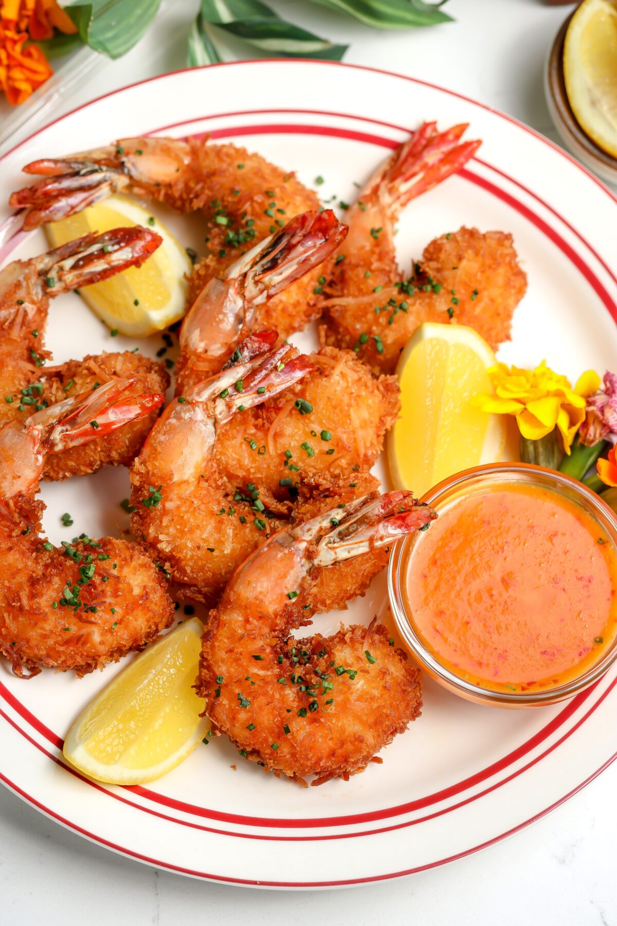 Crispy coconut shrimp with a sweet and spicy chili sauce sitting next to it and garnished with a lemon.