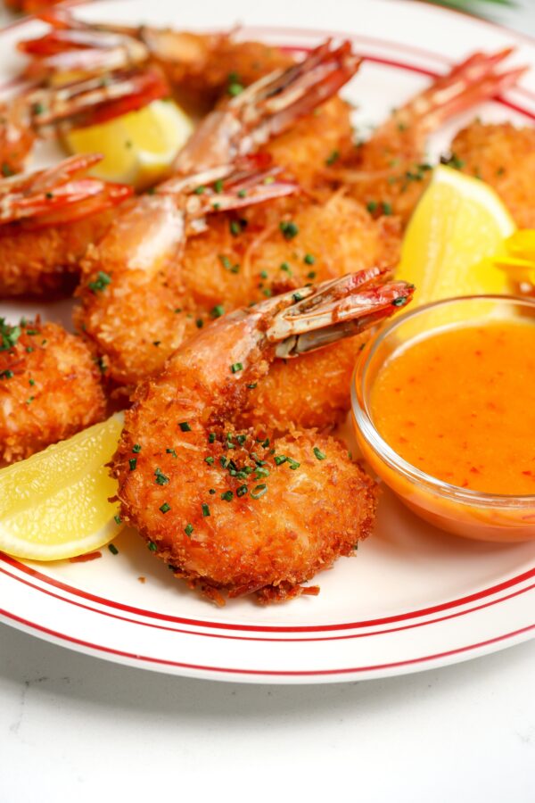 Crispy coconut shrimp with a sweet and spicy chili sauce sitting next to it and garnished with a lemon.