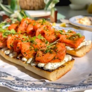 smoked salmon that has been marinated on top of a delicious whipped cheese mixture and then place on a baguette to make a Tartine sitting on a plate.