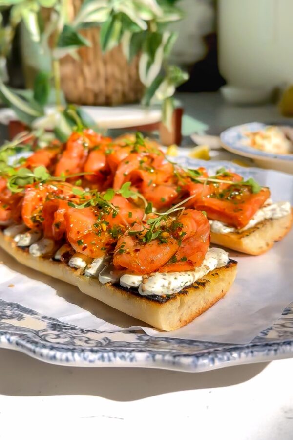 smoked salmon that has been marinated on top of a delicious whipped cheese mixture and then place on a baguette to make a Tartine sitting on a plate.