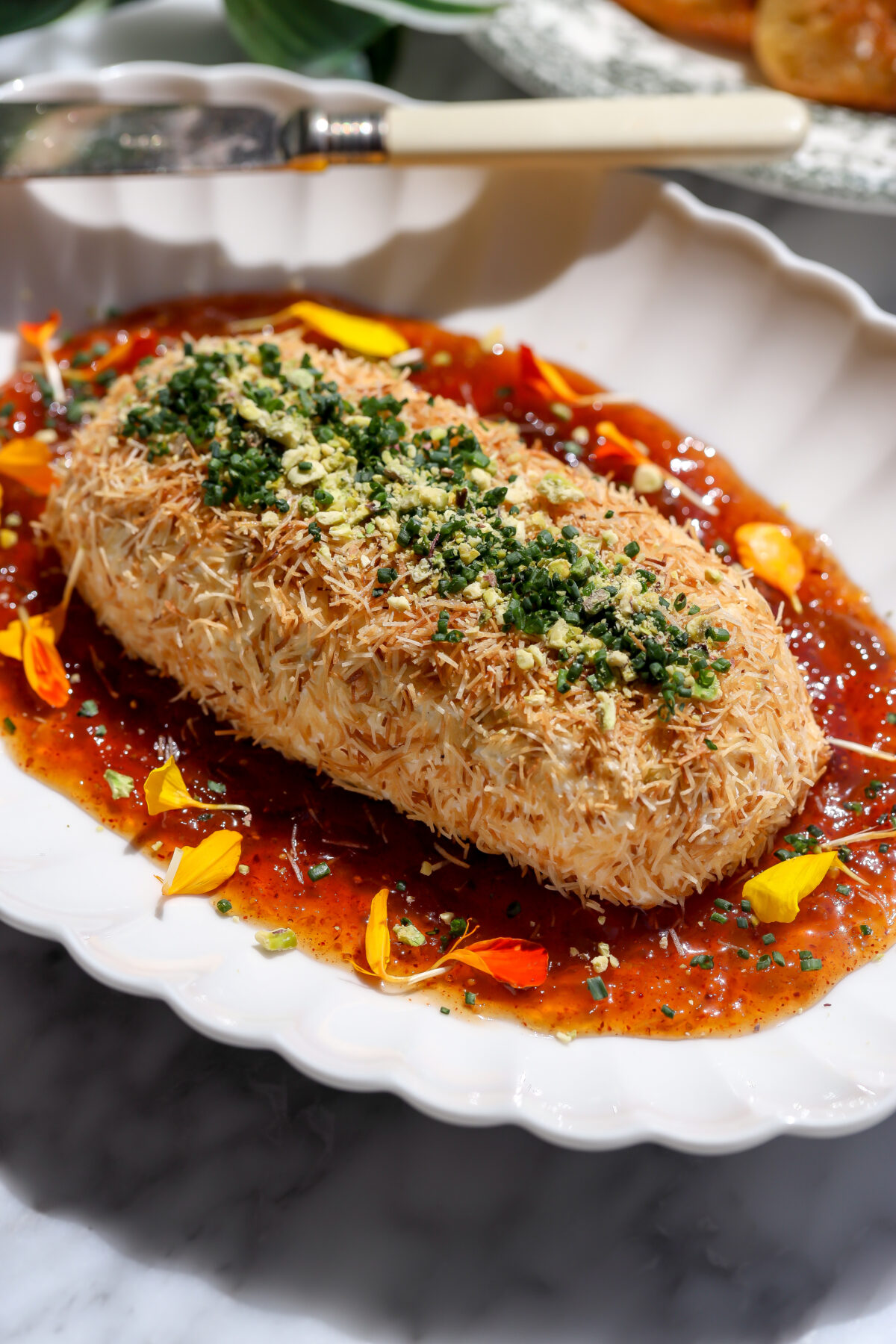 A recipe for whipped feta and cream cheese with a chipotle fig jam inside, coated in toasted kataifi on a plate.
