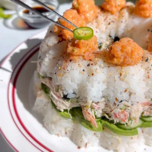 Crab tampico sushi bundt cake topped with piped spicy salmon dollops, sliced serranos, and shichimi togarashi.