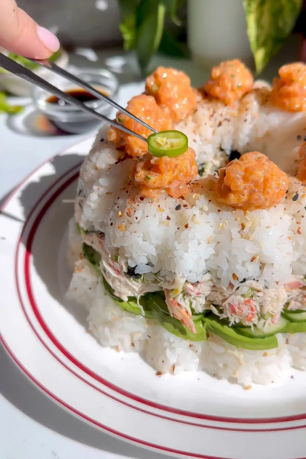 Crab tampico sushi bundt cake topped with piped spicy salmon dollops, sliced serranos, and shichimi togarashi.