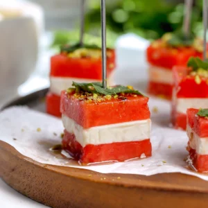 Close-up of a watermelon feta bite on a skewer with hot honey balsamic glaze, a fresh mint leaf, and crushed pistachios.