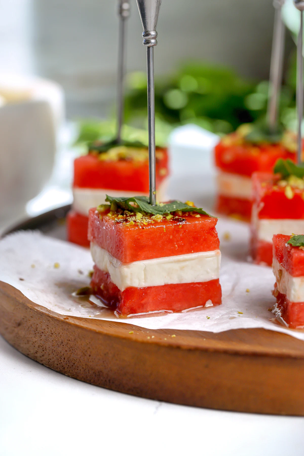 Close-up of a watermelon feta bite on a skewer with hot honey balsamic glaze, a fresh mint leaf, and crushed pistachios.