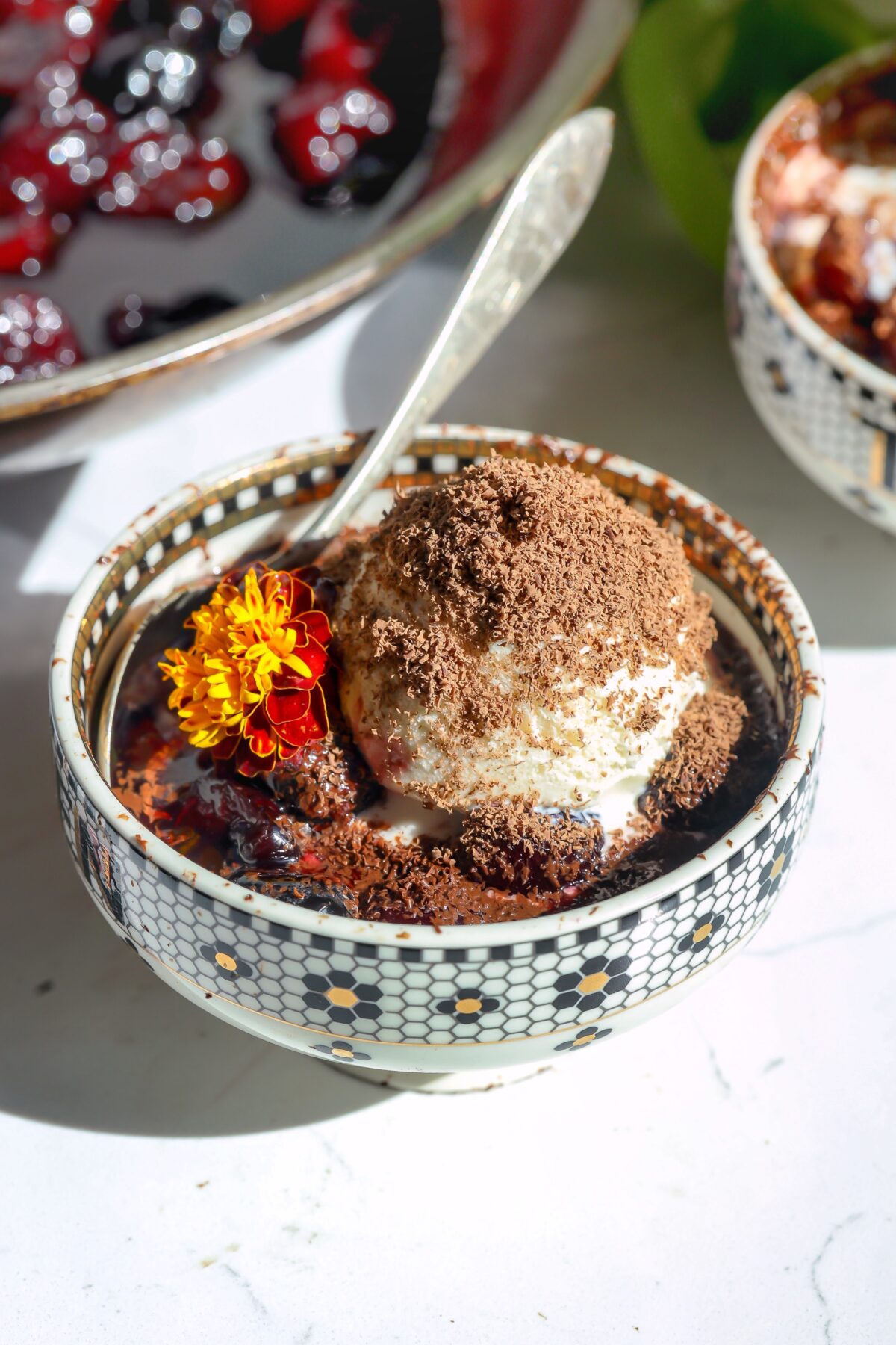 cherries jubilee with ice cream topping and shaved chocolate shavings in a bowl with a spoon.