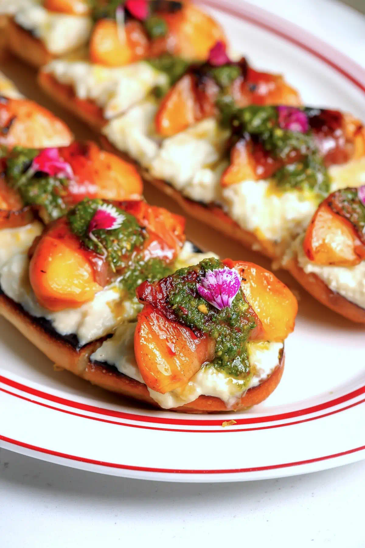 Grilled peach and prosciutto tartine with stracciatella and pistachio herb sauce on a red-rimmed platter