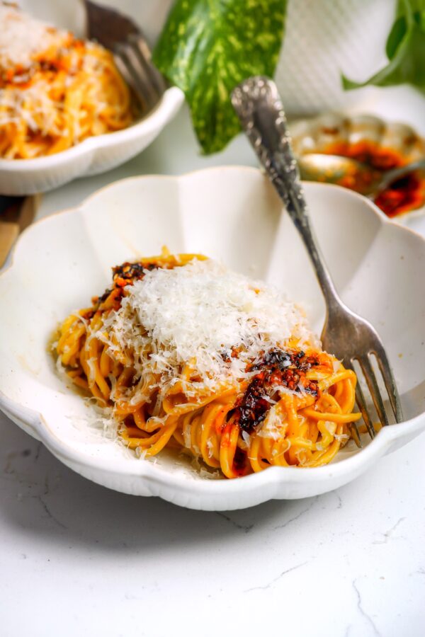Spicy Carbonara style spaghetti in a bowl with parm cheese on top and a fork next to it.