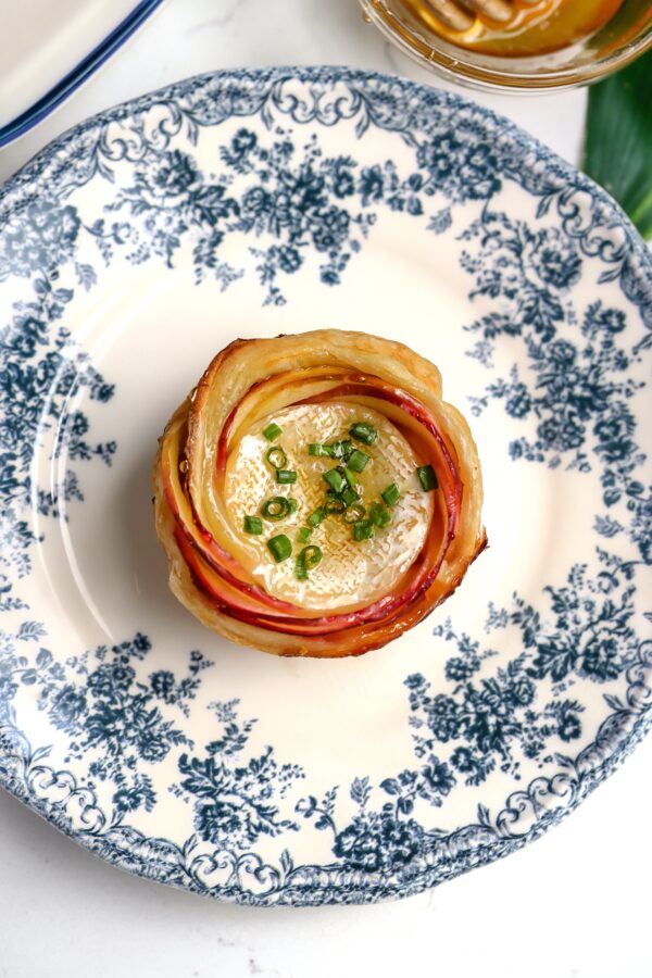 A puff pastry shaped into a rosette with apples wrapped around brie bites and topped with honey and chives.