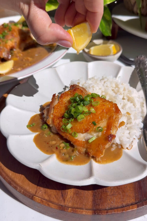 A recipe for Crispy Lemon Scallion Chicken thighs on a plate with rice on the side and sauce on top.