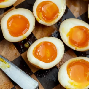 A recipe for perfectly cooked soft-boiled jammy eggs cut in half and ready to be placed in a ramen soup.