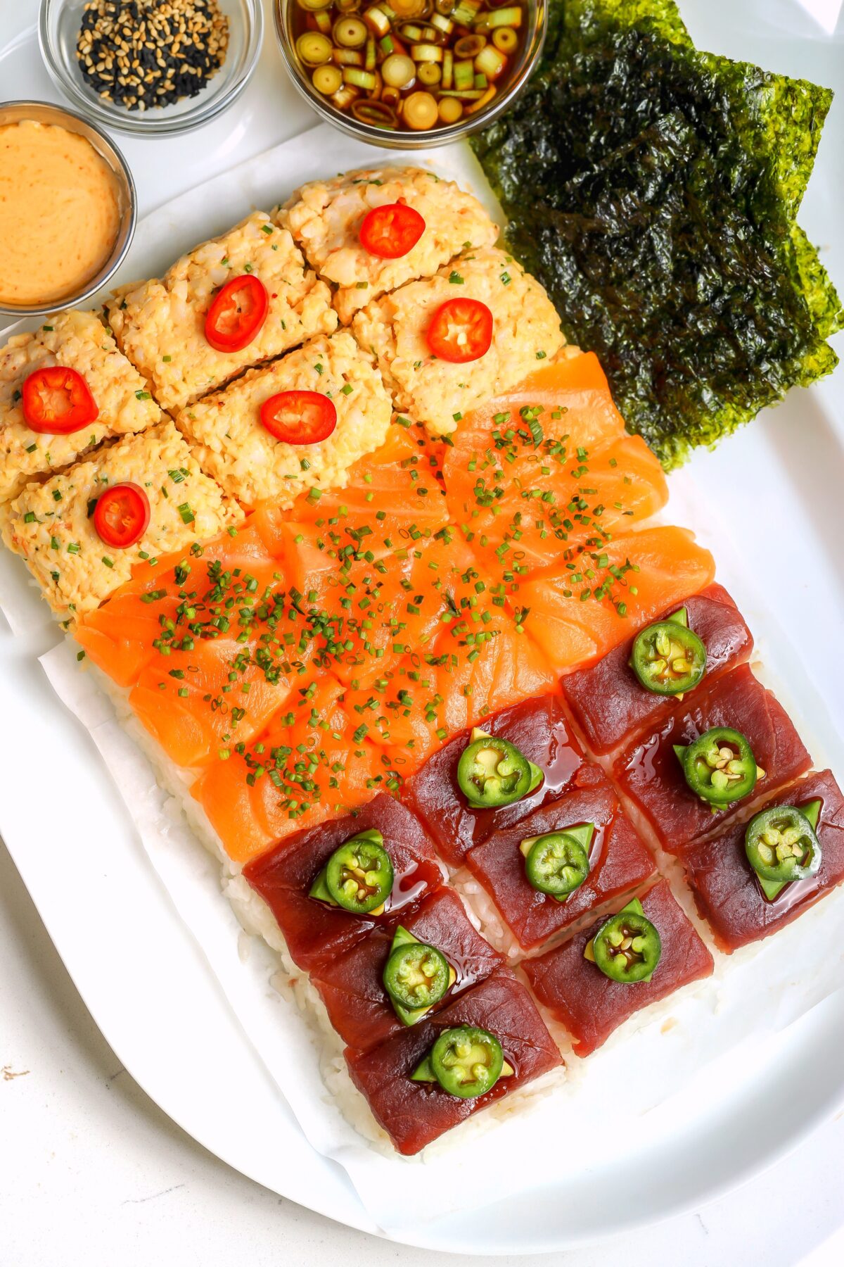 Nigiri-style sushi board with rice on the bottom and three different toppings, spicy crab, salmon and bluefin tuna. On a platter with different sauces on the side.