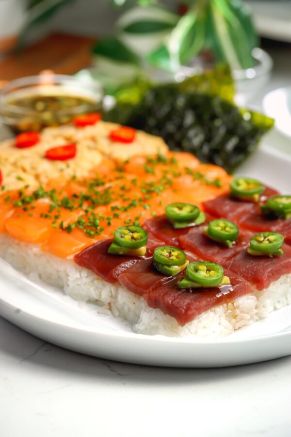 Nigiri-style sushi board with rice on the bottom and three different toppings, spicy crab, salmon and bluefin tuna. On a platter with different sauces on the side.