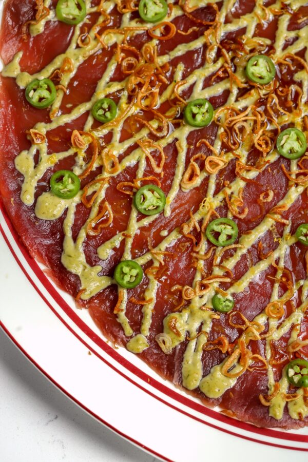 An Italian seafood appetizer of Tuna Carpaccio with yuzu mayo and Serranos on top.