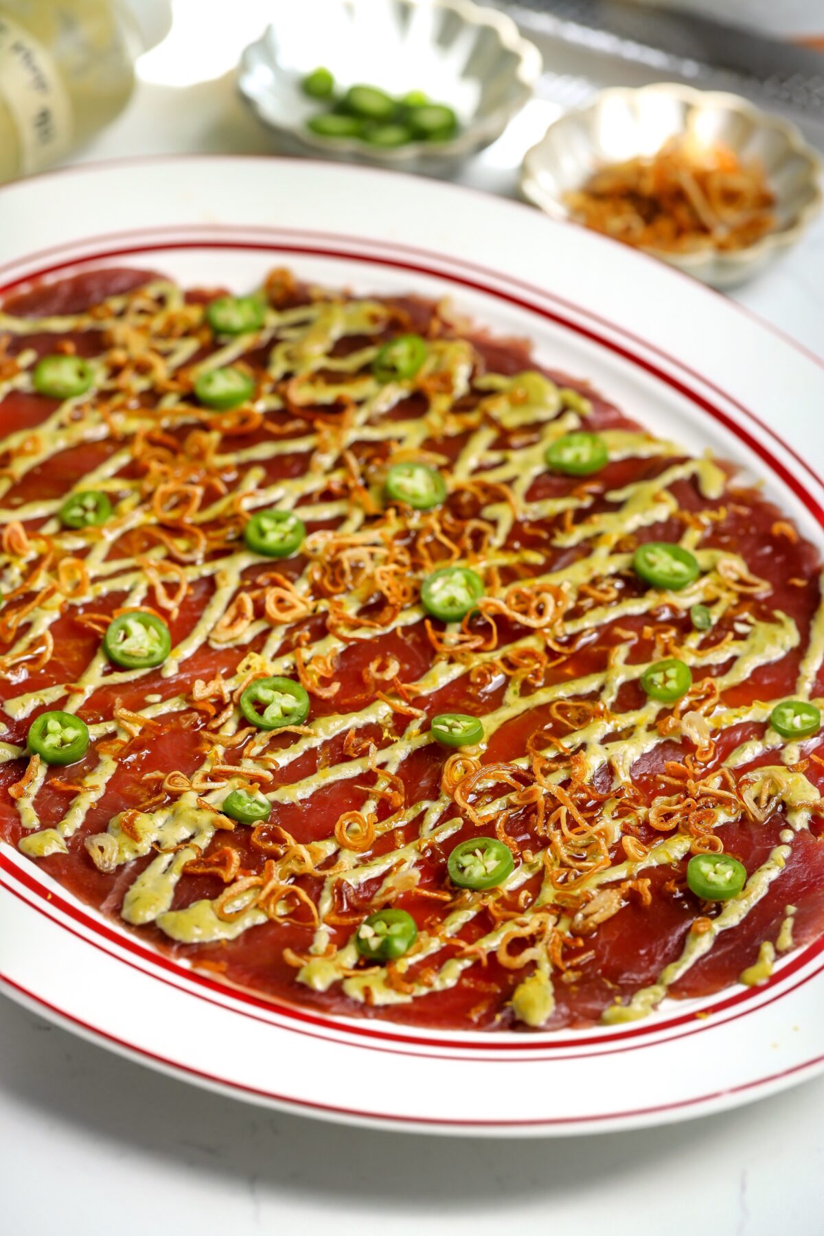An Italian seafood appetizer of Tuna Carpaccio with yuzu mayo and Serranos on top.