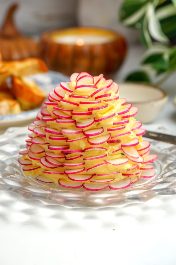 A whipped butter with chives and flaky salt with thin slices of radishes all around sitting on a plate.