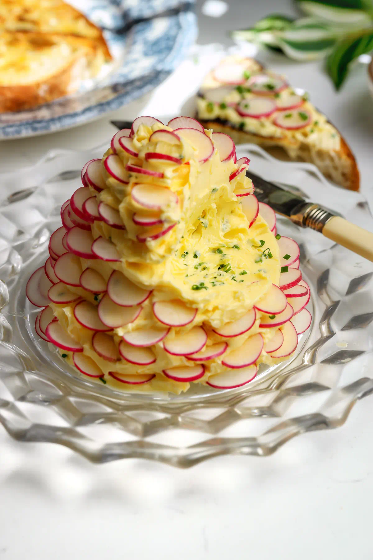 A whipped butter with chives and flaky salt with thin slices of radishes all around sitting on a plate. A piece is missing where the toast was dipped in.