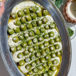This is a blue cheese and cream cheese dip with a bunch of other savory seasonings spread on a plate and topped with blue cheese stuffed olives, the perfect dirty martini the perfect dirty martini easy make-ahead appetizer.