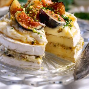 Close-up of creamy brie layered with fig jam and chopped pistachios, ready to top with honey. The perfect holiday appetizer.