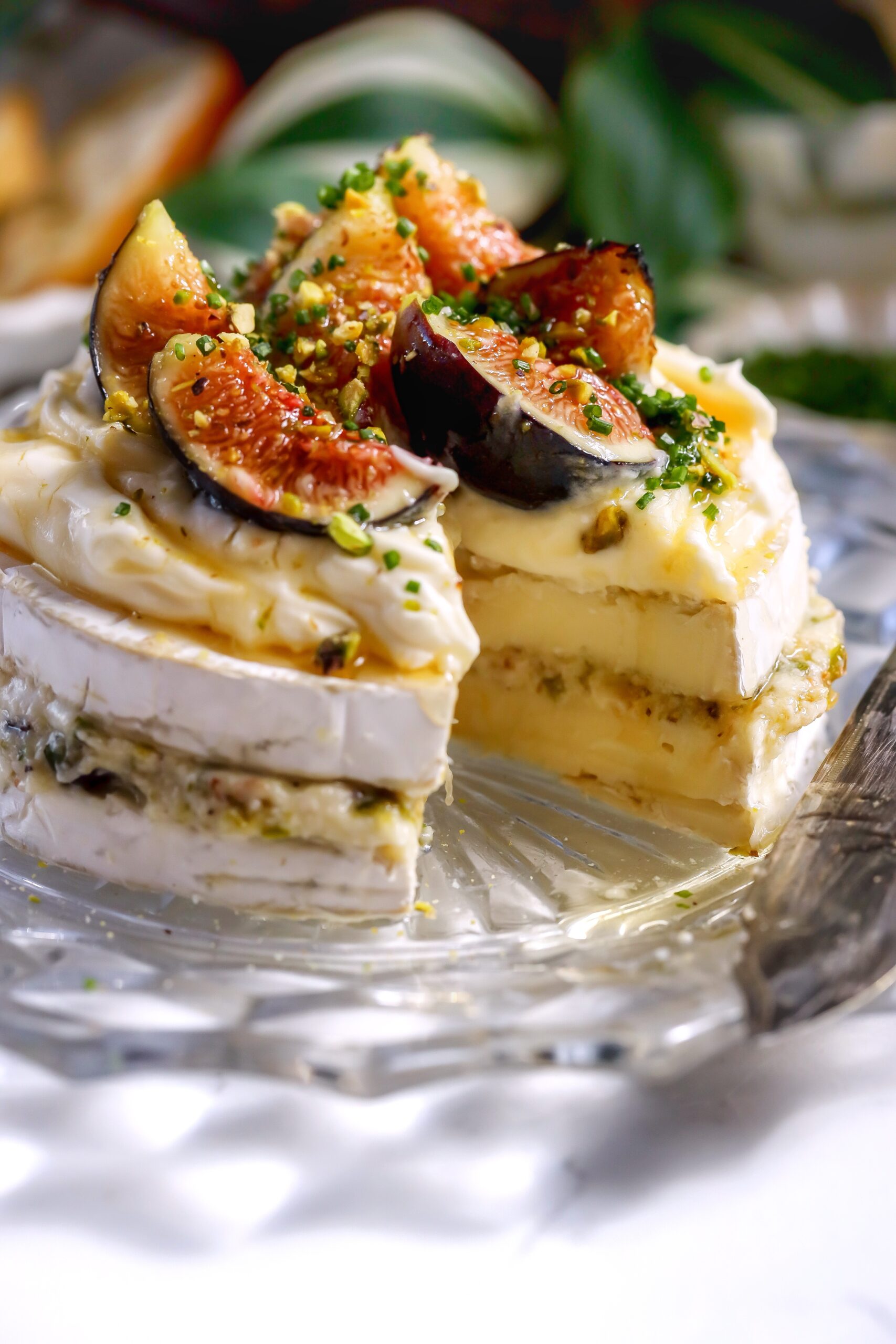 Close-up of creamy brie layered with fig jam and chopped pistachios, ready to top with honey. The perfect holiday appetizer.