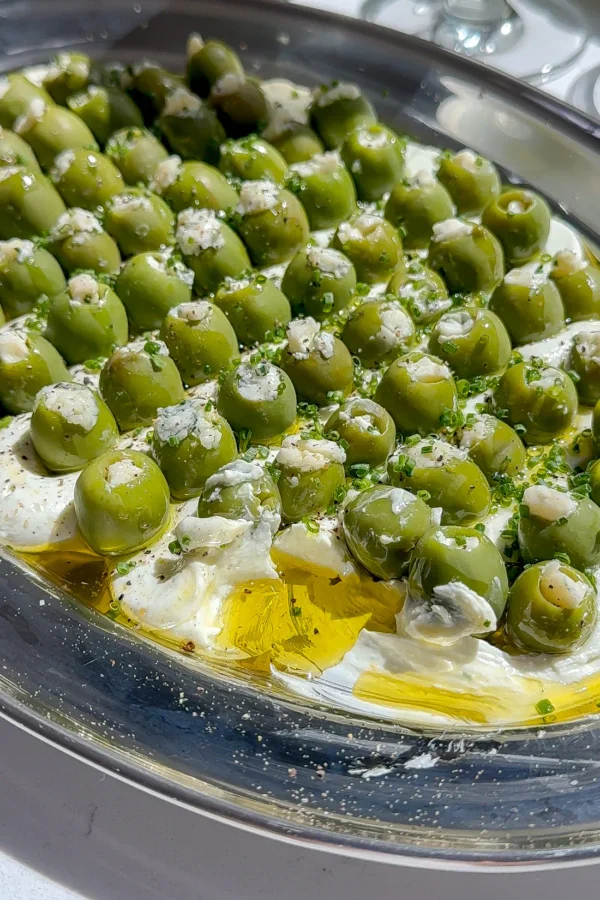 This is a blue cheese and cream cheese dip with a bunch of other savory seasonings spread on a plate and topped with blue cheese stuffed olives, the perfect dirty martini easy make-ahead appetizer.