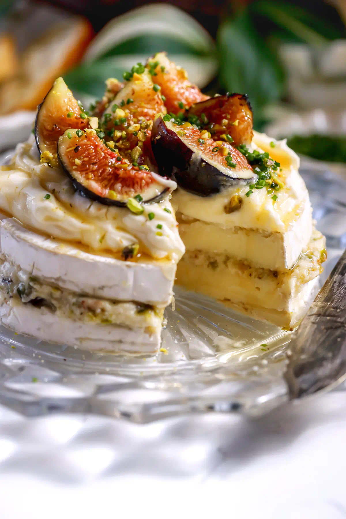 layered brie wheel with pistachios and fig jam. Topped with fresh figs and honey. A slice is taken out to show the brie cake layers.