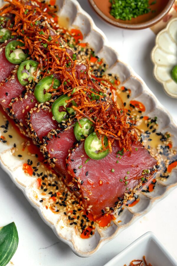Close-up of sesame-crusted tuna crudo drizzled with white soy ponzu and topped with crispy carrot threads.