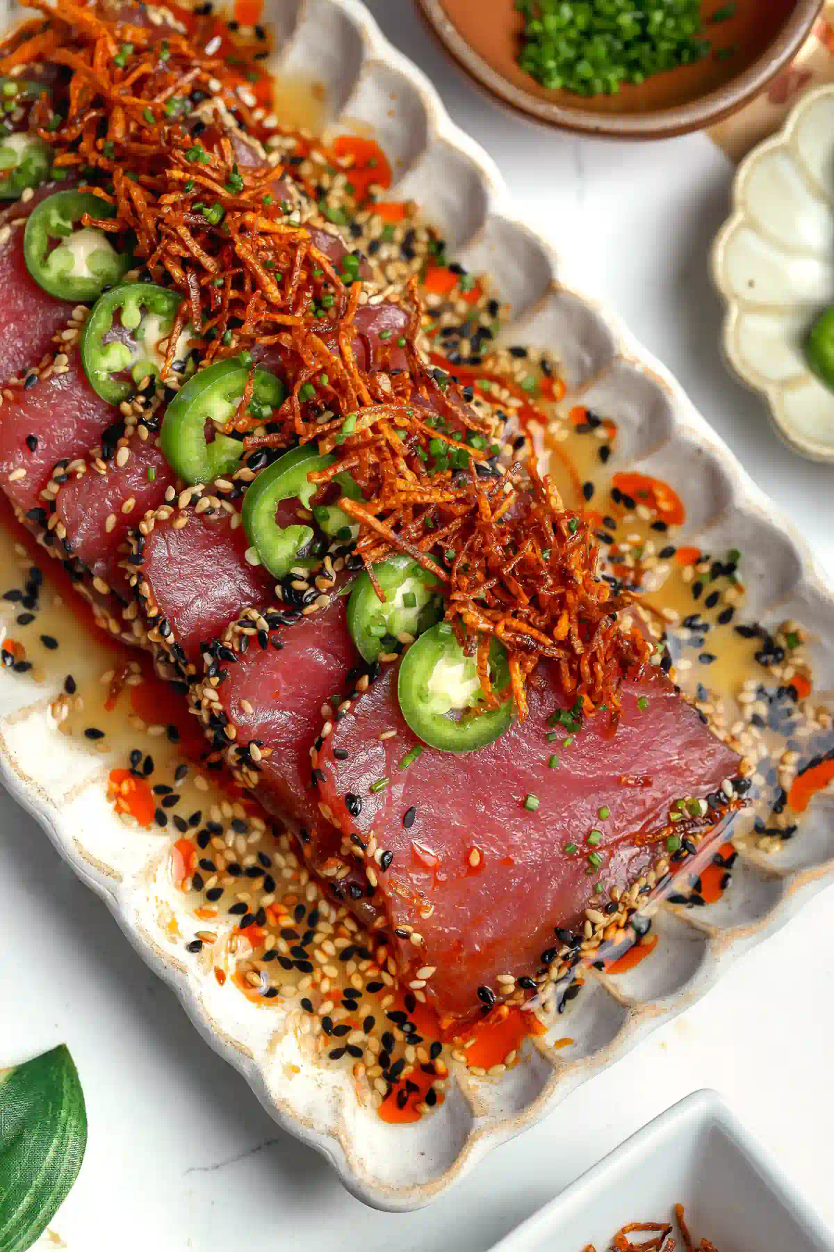 Close-up of sesame-crusted tuna crudo drizzled with white soy ponzu and topped with crispy carrot threads.