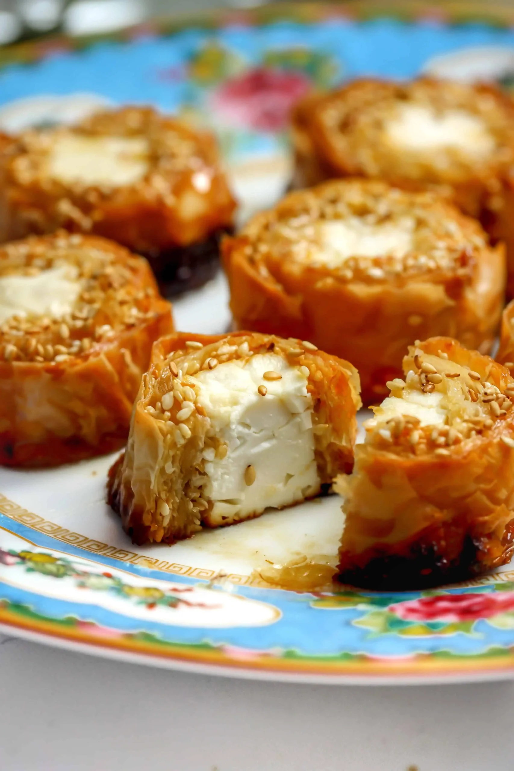 Baked feta phyllo bites with honey butter and sesame, flaky golden layers on a floral plate