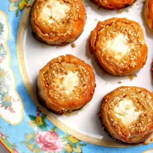 Overhead view of golden baked feta phyllo bites topped with sesame on a blue floral plate