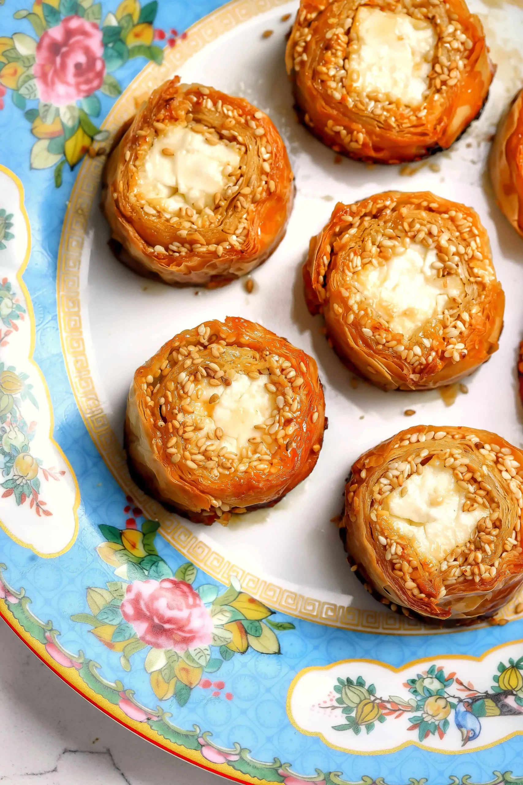 Overhead view of golden baked feta phyllo bites topped with sesame on a blue floral plate