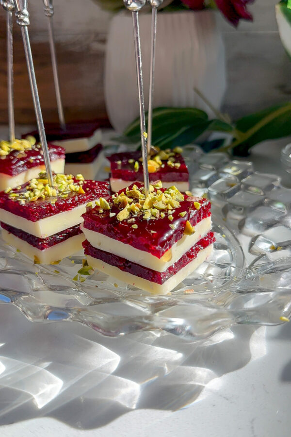 Layered cranberry jelly cheddar cheese appetizer bites topped with crushed pistachios, served on a clear glass plate with silver picks. cranberry jelly for cheese
