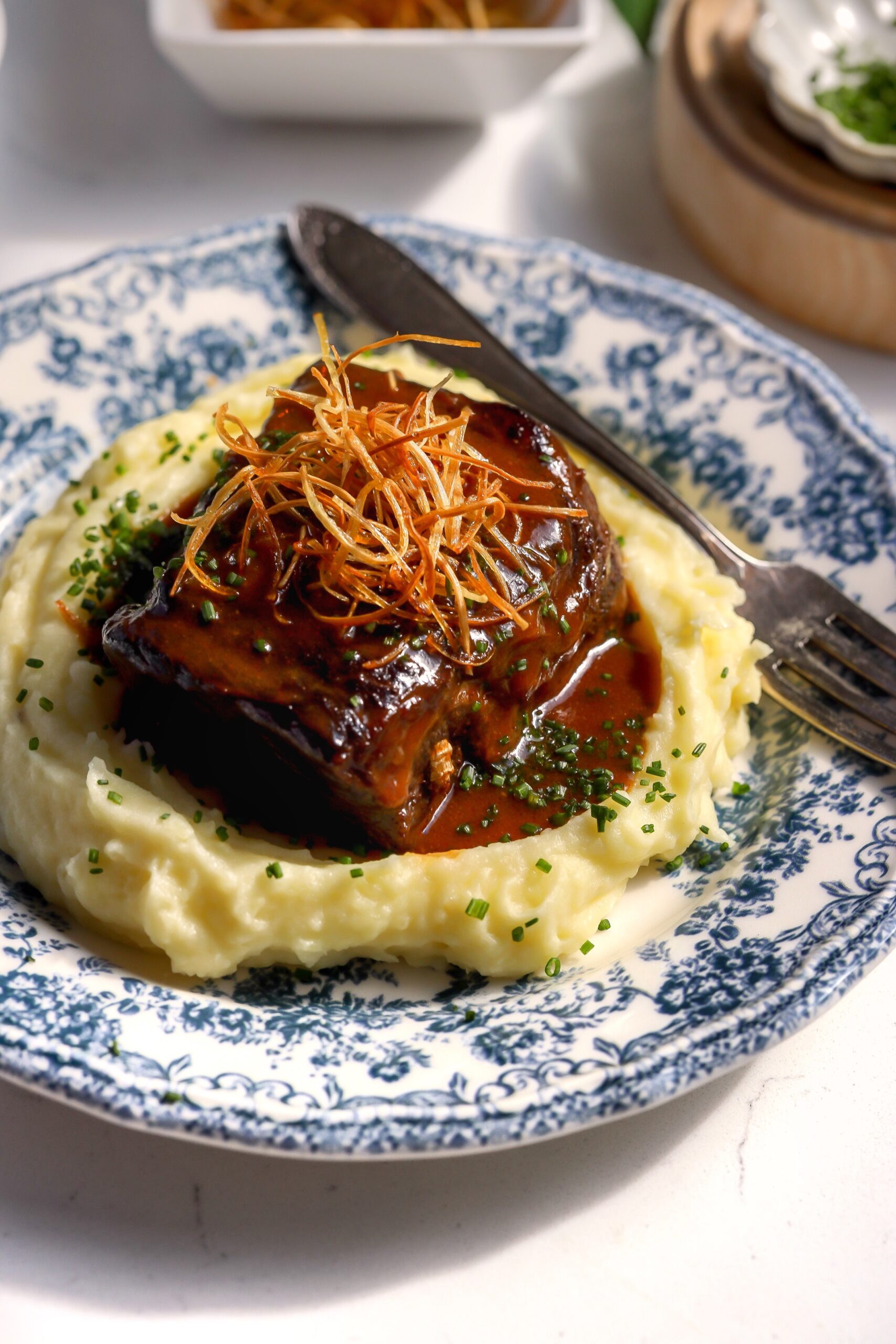 Boneless braised beef recipe with mashed potatoes on a blue floral plate