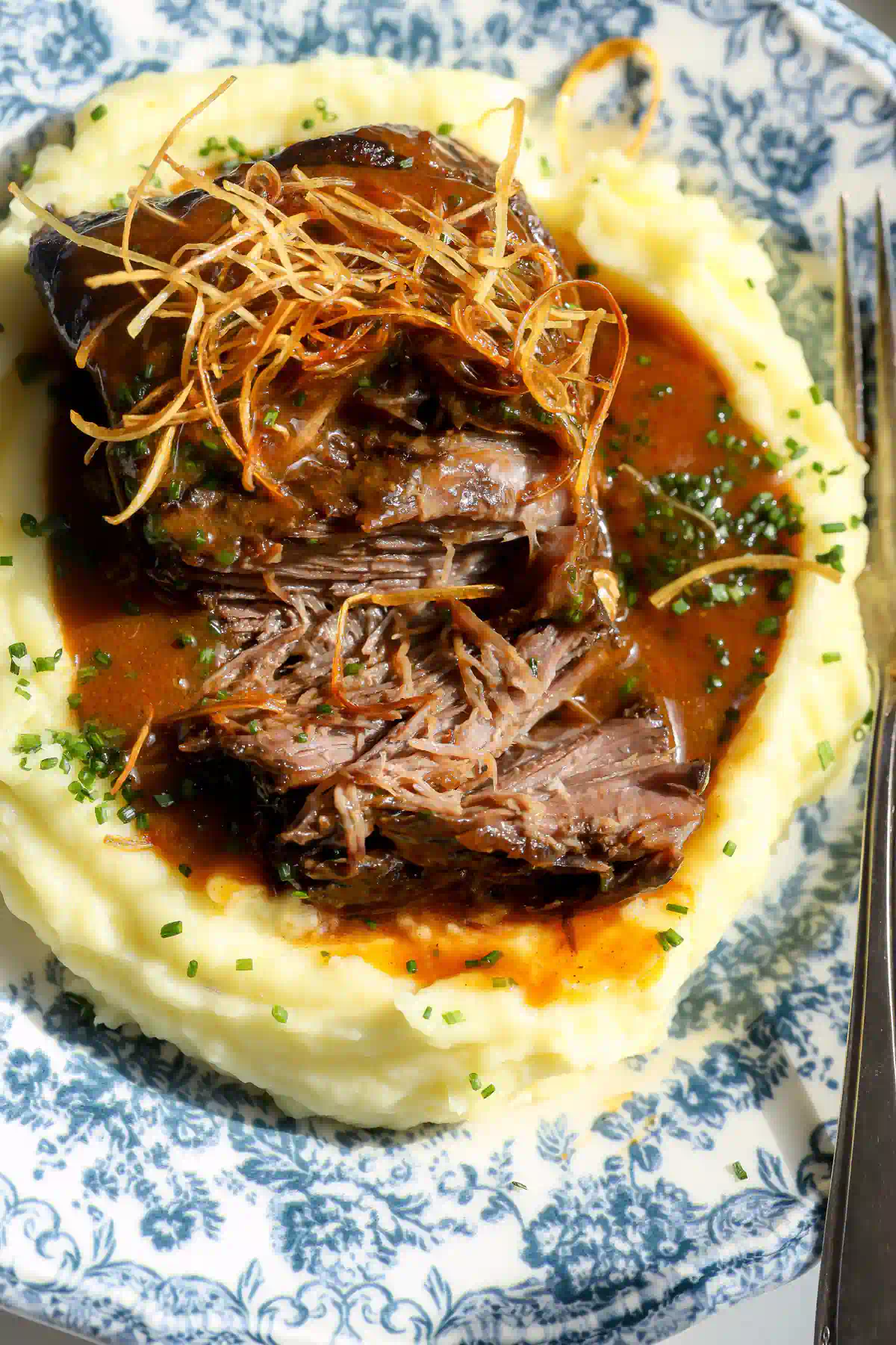 Close-up of miso maple short ribs on mashed potatoes with glossy miso glaze, crispy leeks, and chives.