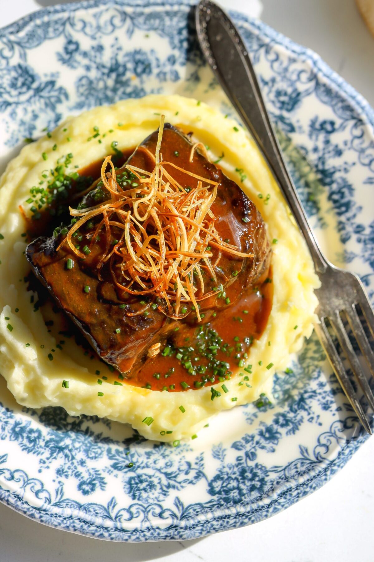 Miso maple short ribs over mashed potatoes with glossy miso gochujang glaze and crispy leeks on top.