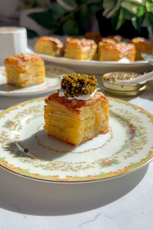 Potato gratin stacks layered and topped with crème fraîche and caviar on a vintage plate