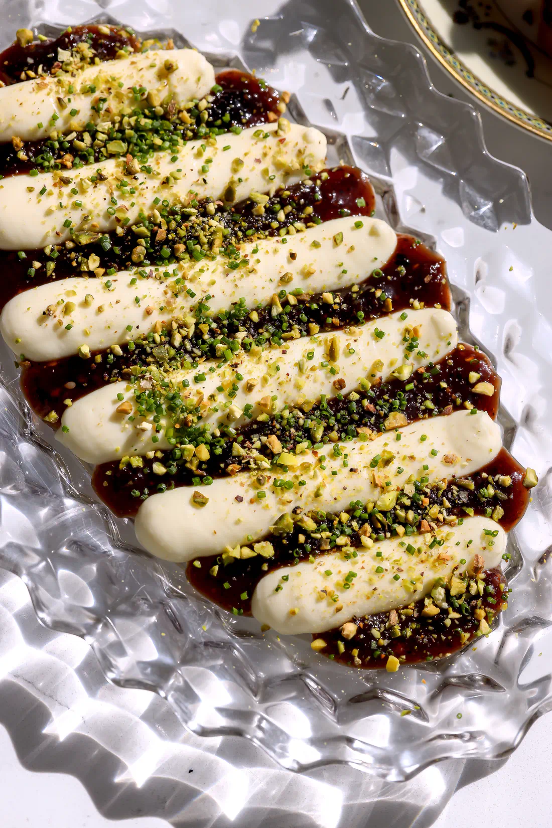 Close-up of whipped brie jam dip topped with chopped pistachios and chives &ndash; creamy cheese and spicy berry jam appetizer on a glass platter.