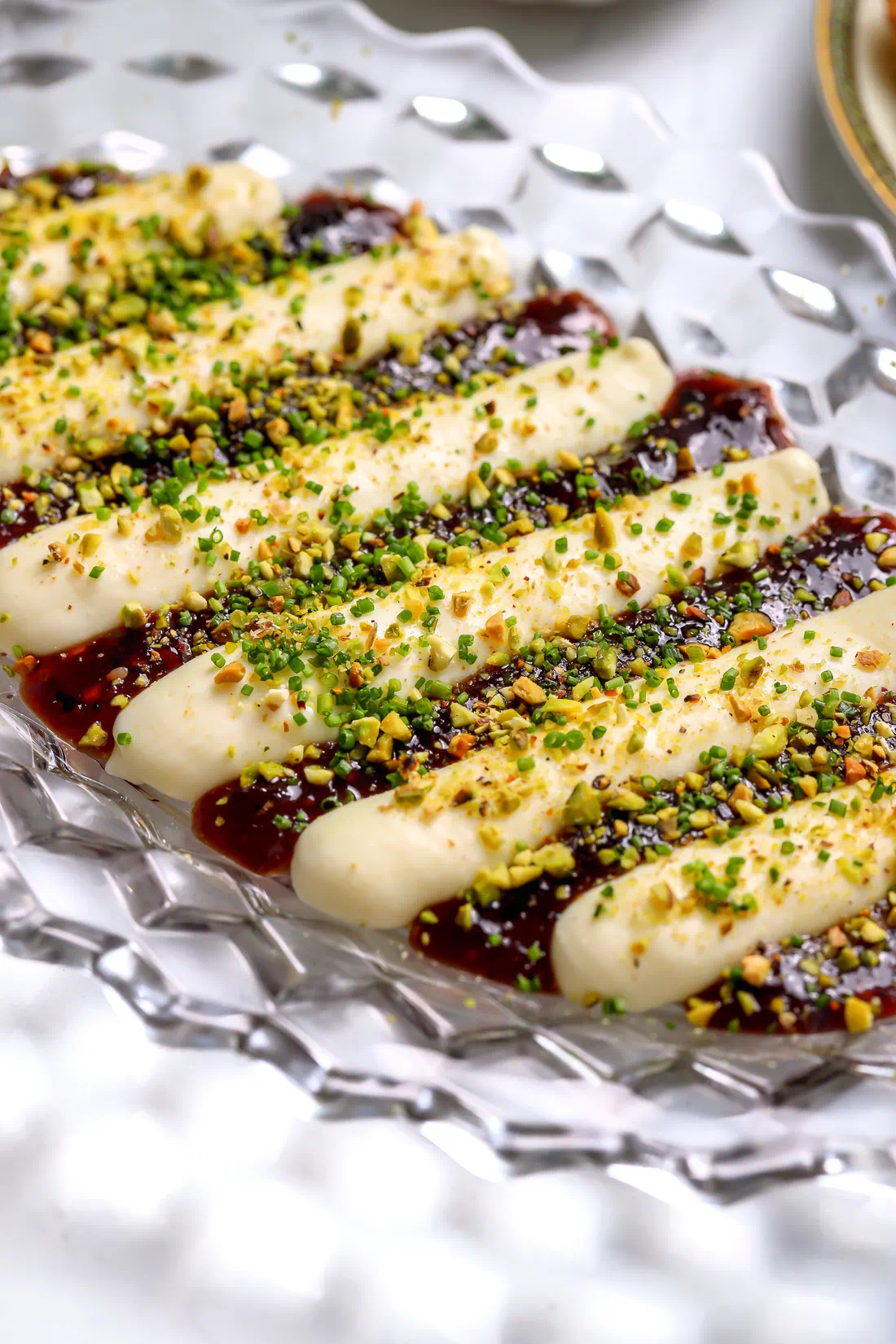 Whipped brie jam dip topped with chopped pistachios and chives &ndash; creamy cheese and spicy berry jam appetizer on a glass platter.