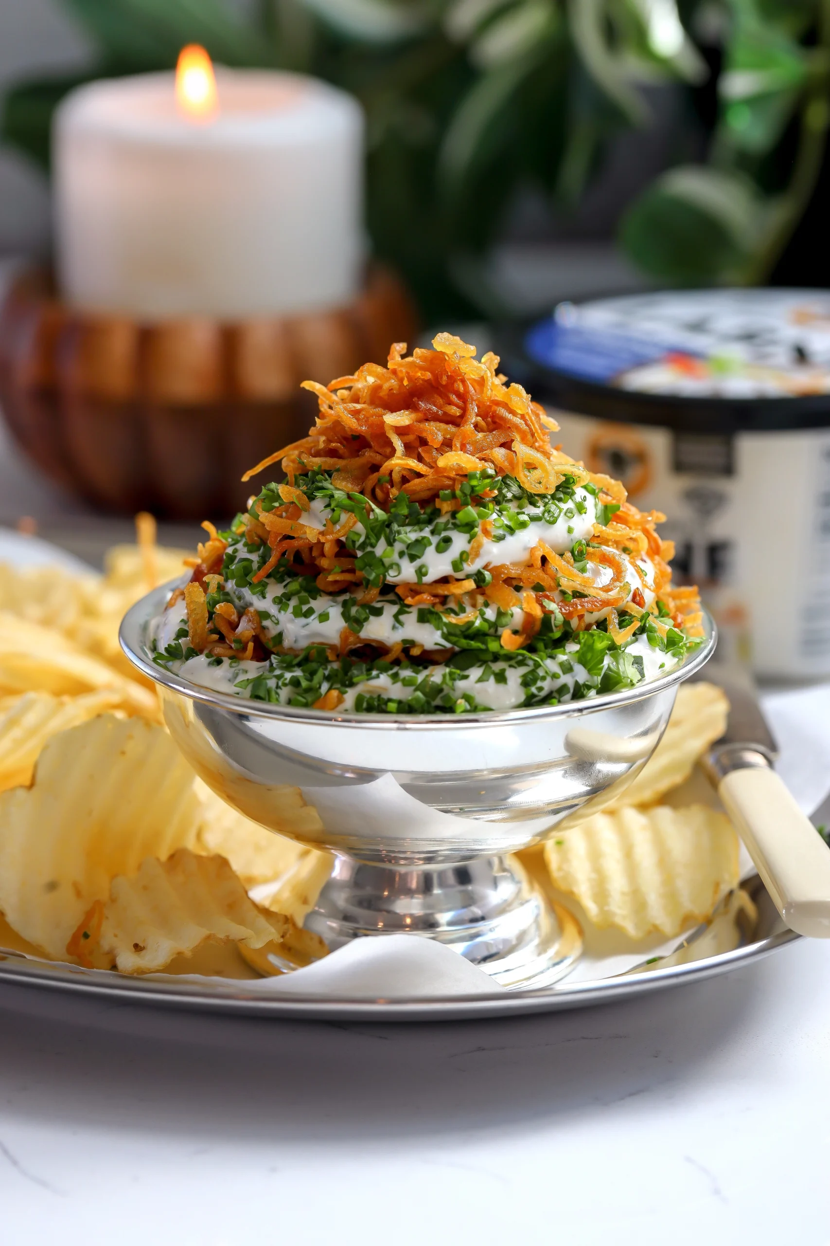 A layered crispy onion and herb dip made with labneh, fresh herbs, and fried onions, served with ridged potato chips