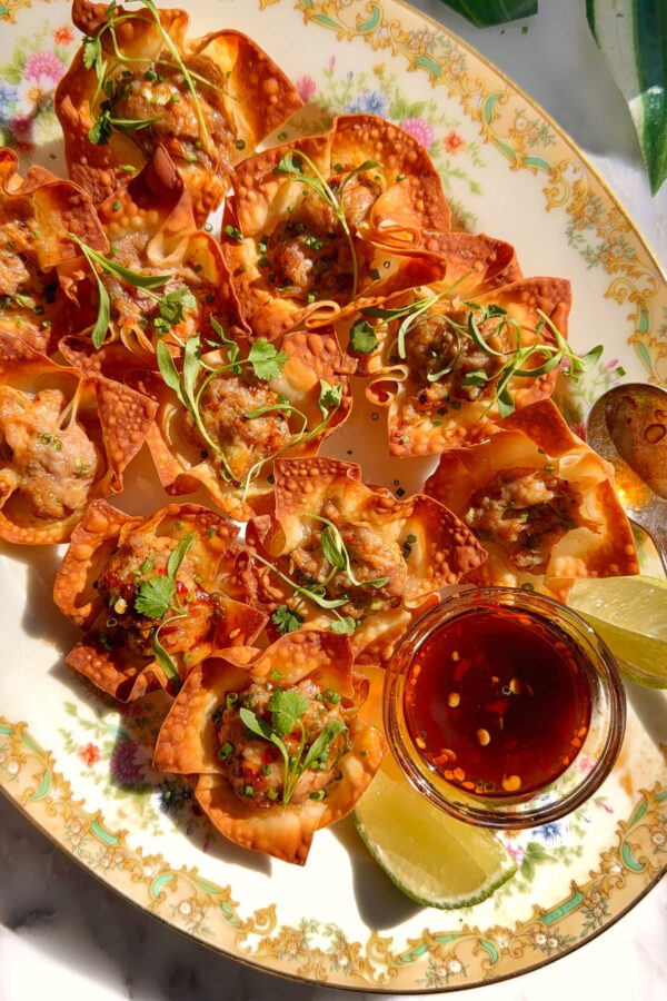 Baked pork and shrimp wonton cups arranged on a platter with dipping sauce and herbs