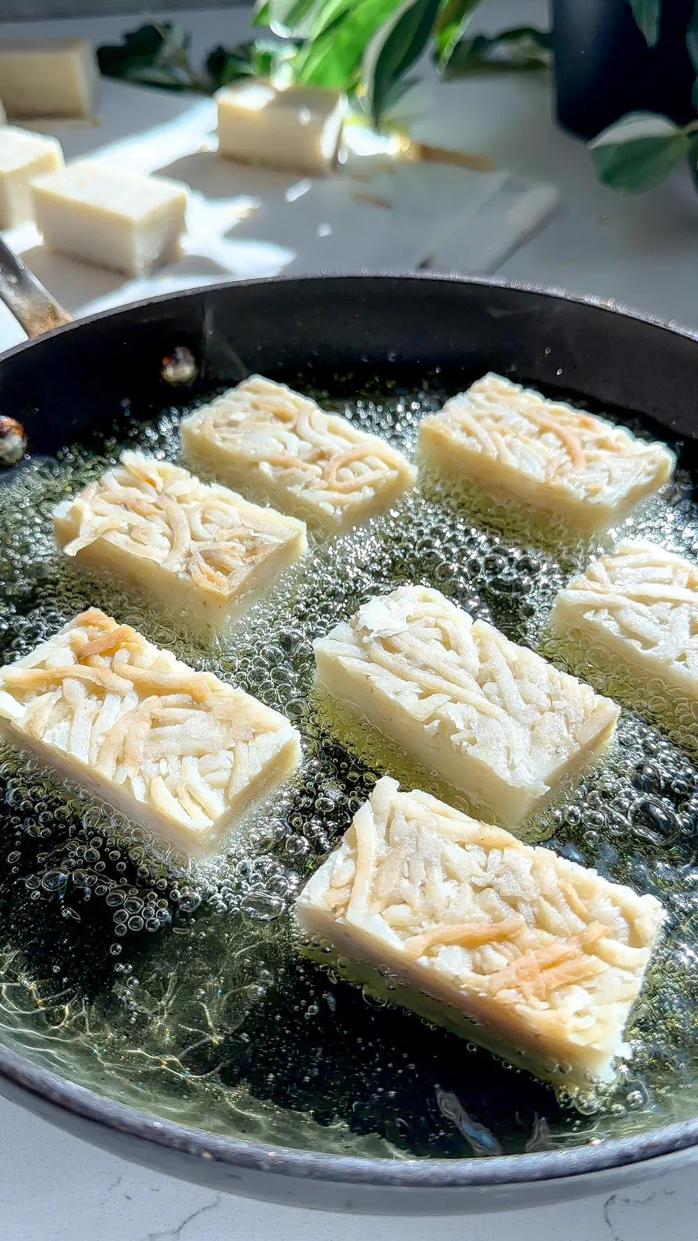 Several pale, rectangular pressed potato bricks frying in a pan of hot oil.