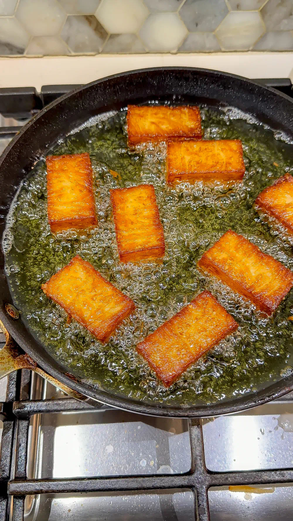 Golden brown, crispy potato bricks being seared in a black skillet with bubbling oil.