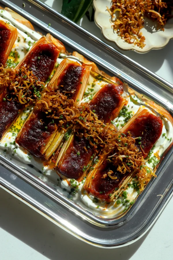 Overhead shot of a silver oval platter with golden roasted leeks stuffed with red nduja and served over whipped labne.