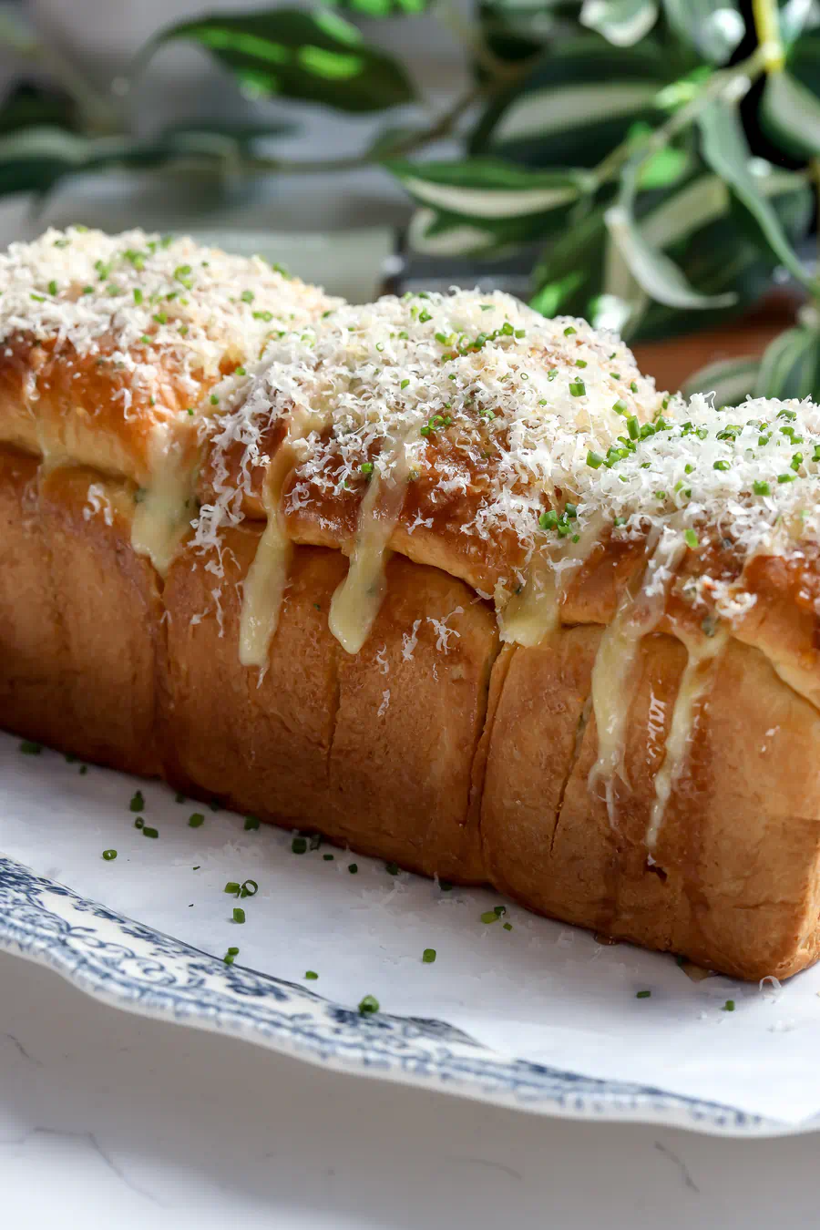 A whole baked cheesy garlic pull-apart brioche loaf stuffed with melted cheese and topped with fresh herbs, sitting on a dark surface.