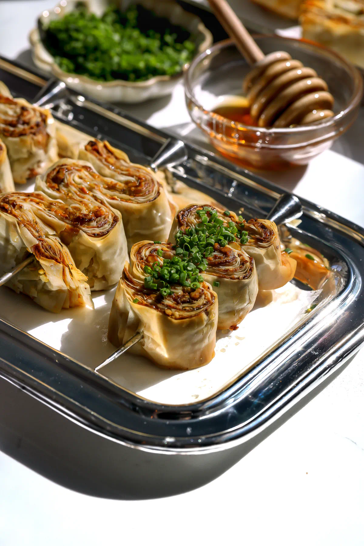 Angled shot of crispy phyllo appetizer skewers served with a side of honey and a wooden dipper.