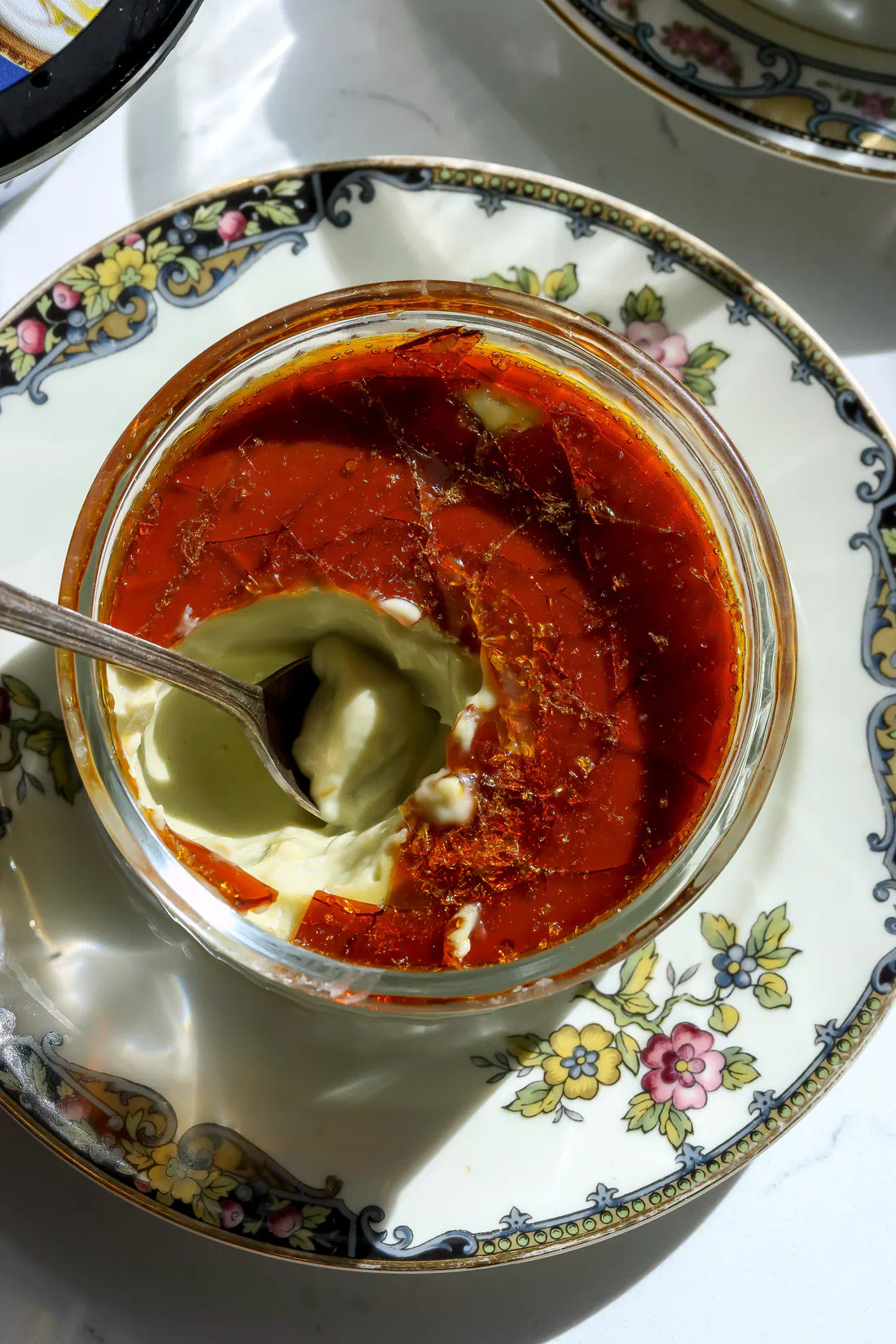 A spoon breaking through the hard caramel shell of a creamy pistachio creme brulee made without a kitchen torch.