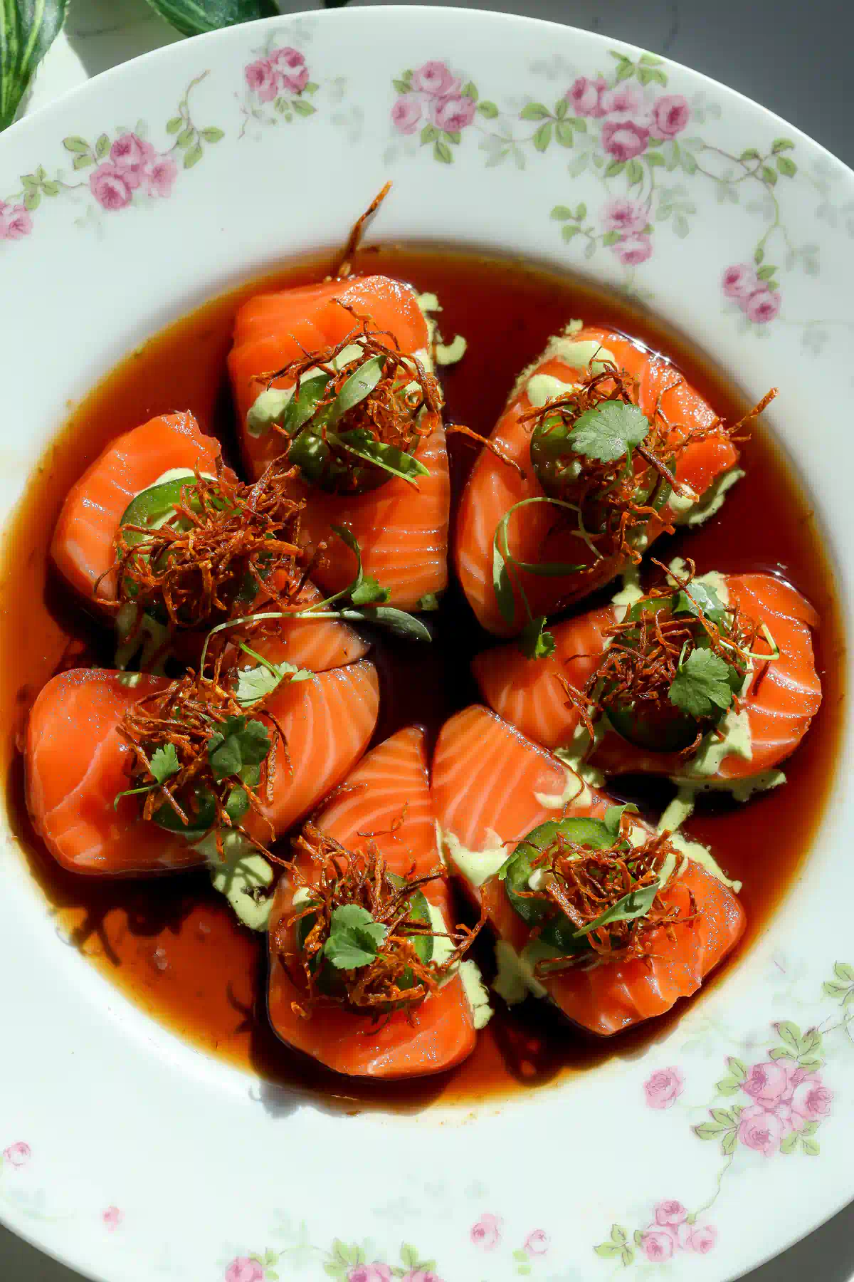 Close up of sweet ponzu salm&oacute;n crudo drizzled with creamy jalape&ntilde;o sauce and topped with crispy fried carrot matchsticks.