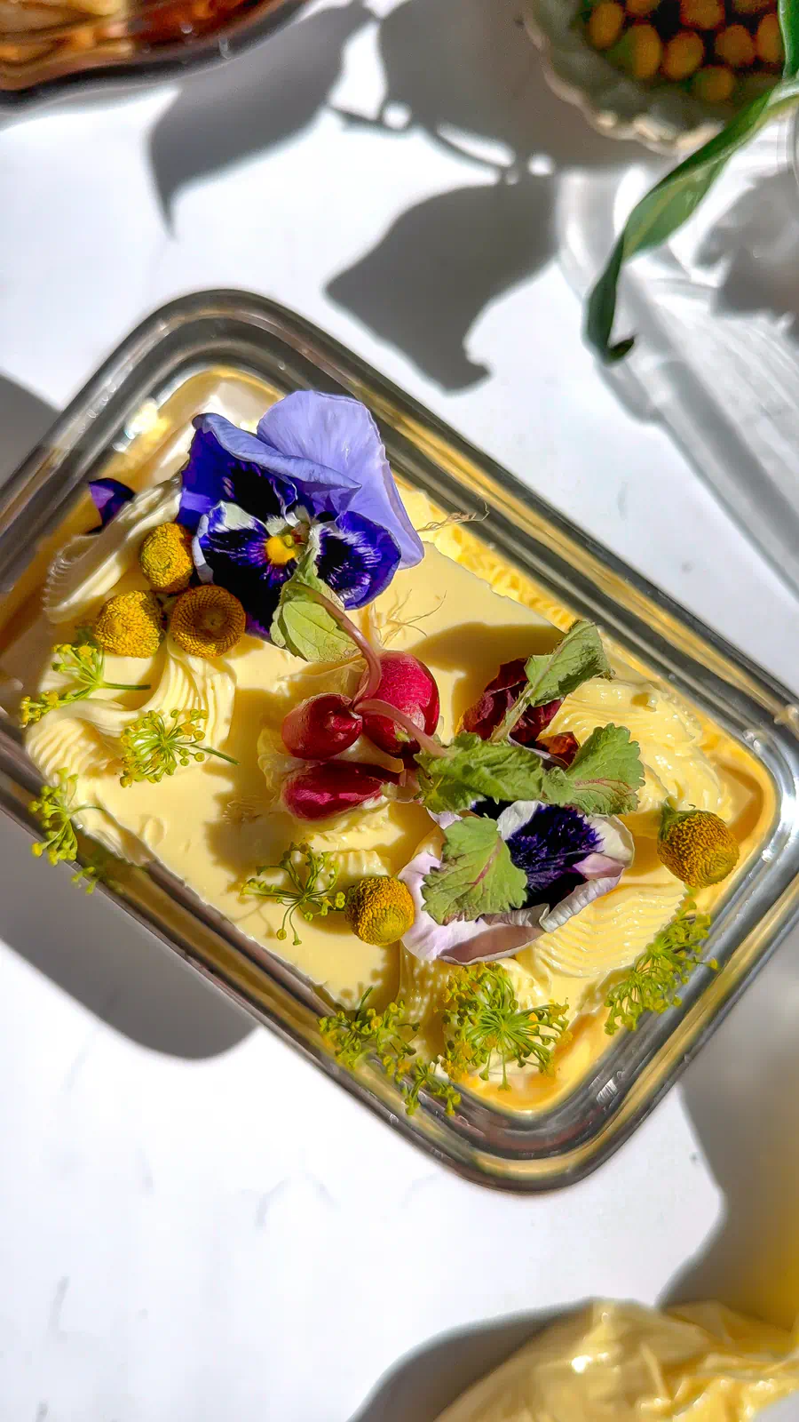 A top-down view of a savory butter cake topped with fresh radishes, purple pansies, and bright yellow dill flowers.